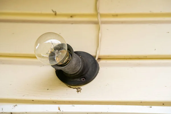 Żarówkowa żarówka z pajęczynami i brudem oświetla białą ścianę przy wejściu do domu. Początek sezonu letniego domku letniskowego — Zdjęcie stockowe