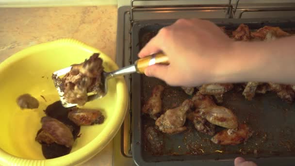 Las alas de pollo picante recién horneadas se transfieren de una bandeja para hornear caliente a un tazón de salsa barbacoa — Vídeos de Stock