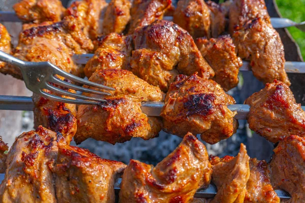 Hombre usando un tenedor comprueba la preparación del kebab carne marinada en pinchos en la parrilla — Foto de Stock