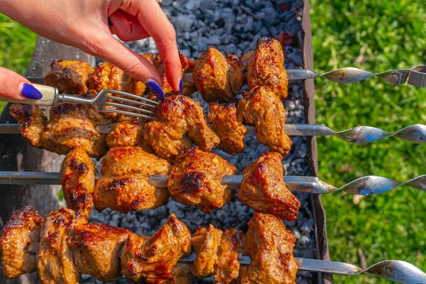 Una chica que usa un tenedor comprueba la preparación del kebab carne marinada en pinchos en la parrilla — Foto de Stock