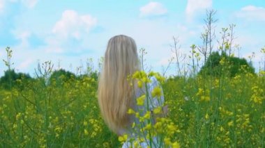 Beyaz elbiseli güzel bir kız başını çevirir uzun dalgalı saçlarıyla yaz aylarında çiçek açan bir tecavüz tarlasında