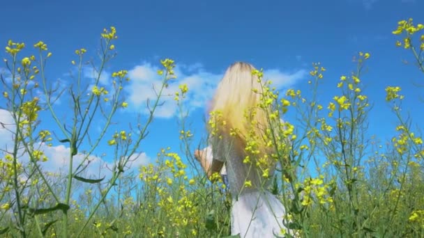 Молода красива дівчина ховається за солом'яним капелюхом і фліртує в квітковому полі ріпаку влітку — стокове відео