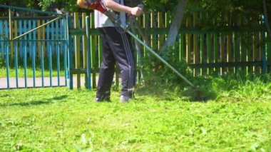 Elinde benzin biçme makinesiyle evin önünde çim biçen bir işçi. Bir adamın elindeki çim biçme makinesi. Bahçıvan çimenleri kesiyor..