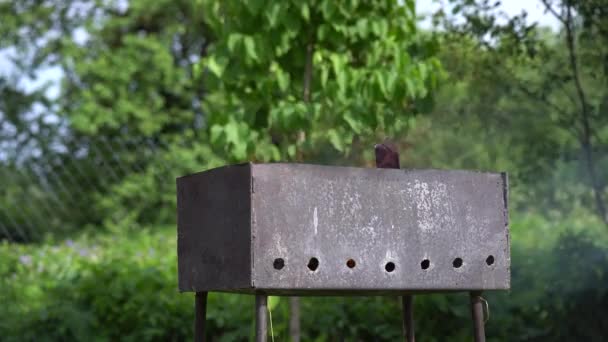 Een man gooit brandhout in een rookenrooster in zijn achtertuin — Stockvideo