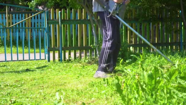 Trabalhador com um cortador de gasolina nas mãos, cortando grama na frente da casa. Aparador de relva nas mãos de um homem. Jardineiro cortando a grama verde. — Vídeo de Stock