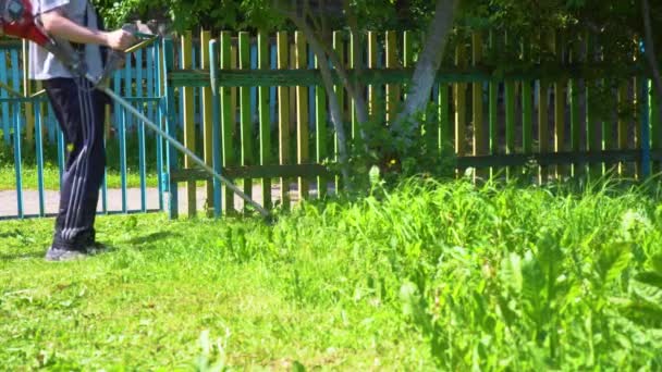 Grästrimmer i händerna på en man. Arbetare med en bensingräsklippare i händerna, klipper gräs framför huset. Trädgårdsmästare skär det gröna gräset. — Stockvideo