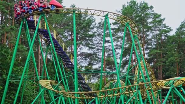 American Roller Coaster em um parque de diversões, uma cabine com pessoas corre ao longo de uma montanha-russa alta em um parque de atração — Vídeo de Stock