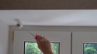 Bir kadın pencerenin yamaçlarını beyaz boyayla boyuyor, pencere açıklarını silindirle boyuyor, pencere çerçevelerini beyaz boya ile boyuyor.