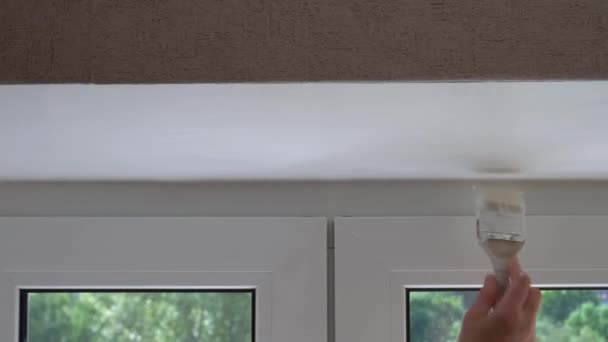 Een vrouw schildert de hellingen bij het raam met witte verf, schildert de raamopeningen met een verfkwast, schildert raamkozijnen met een rol witte verf — Stockvideo