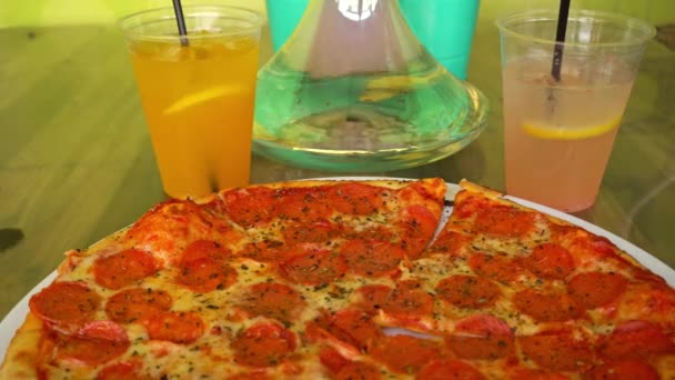 Mens strony bierze kawałek pizzy pepperoni na tle bąbelków hookah i koktajle w ulicznej kawiarni — Wideo stockowe