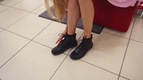 Ragazza con i capelli lunghi cercando su scarpe nuove in un negozio di scarpe, allacciatura scarpe nuove, calzatura camera — Video Stock