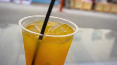 Plastik bardakta buzlu tropikal bir limonata, bir kafede portakal ve narenciye karışımı ve bir yudum alır.