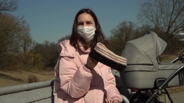 Jonge moeder met een wandelwagen koesterend in de herfstzon en zwaaiend met een gebreide hoofdband — Stockvideo