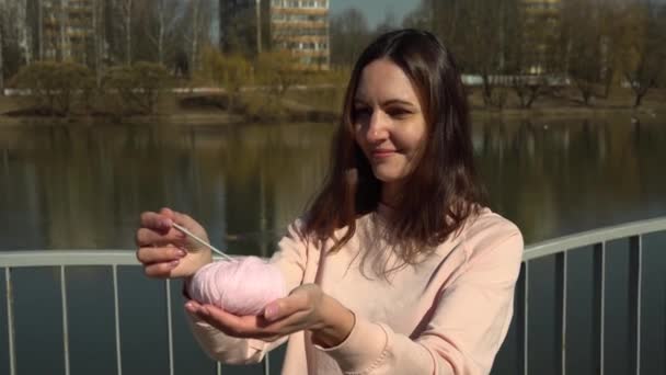 Chica sosteniendo una bola de hilo y un ganchillo gancho durante una sesión de fotos en el terraplén en la ciudad — Vídeos de Stock