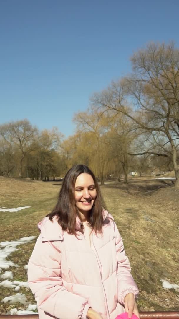 Una chica con una chaqueta rosa lanza una bola de hilos en un parque de primavera de otoño video vertical en cámara lenta — Vídeos de Stock