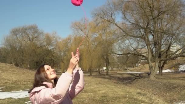 Egy rózsaszín kabátos lány feldob egy gombolyagot egy őszi tavaszi parkban lassított felvételen. — Stock videók