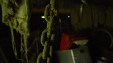 Paslı zincirler tavandan sarkıyor ve terk edilmiş bir bodrumda asılı duruyor. Eski bir ahırda metal bir zincir ve kanca hareketi.