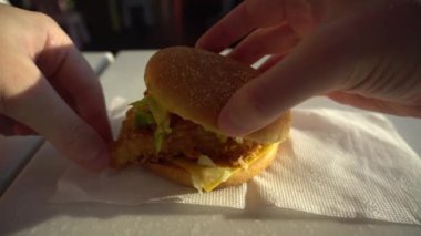 Erkek eller bir fast food kafede hamburger yer, bir adam hamburgeri ısırır ve masaya bırakır.