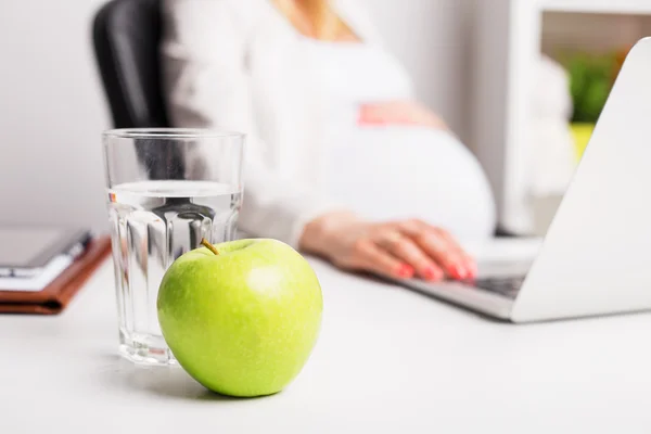 Έγκυος γυναίκα στο γραφείο έχοντας μήλων και νερό — Φωτογραφία Αρχείου
