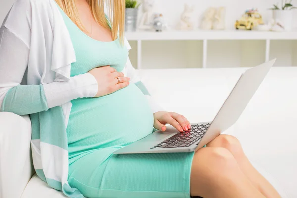 Mulher grávida sentada no sofá e usando laptop — Fotografia de Stock
