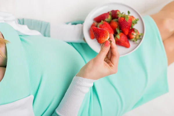 Donna incinta seduta sul divano e mangiare fragole dalla ciotola — Foto Stock