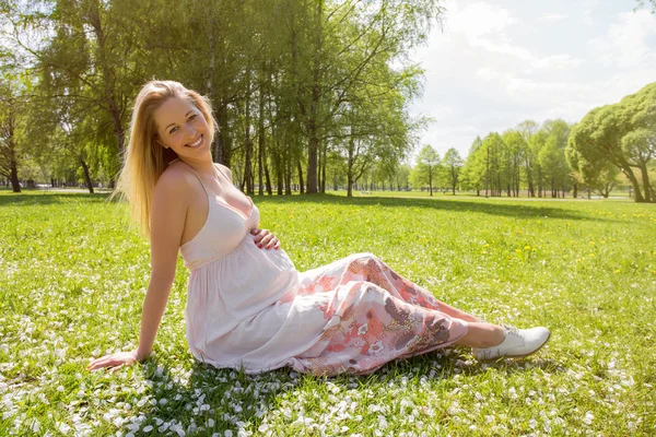 Vacker och gravid kvinna som sitter i gräset — Stockfoto