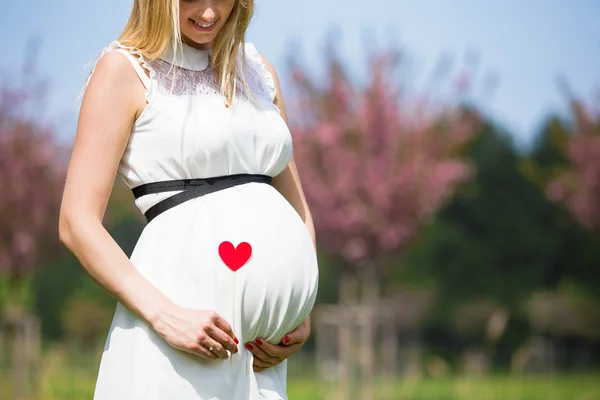 Frau hält ihren Babybauch mit Herzzeichen — Stockfoto
