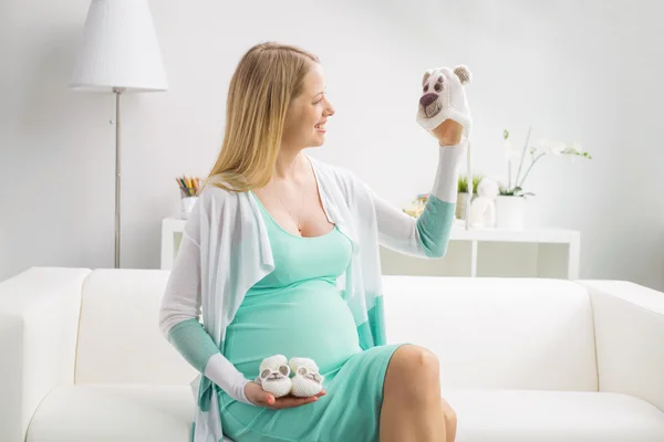 Femme enceinte tenant chapeau et chaussures de bébé — Photo