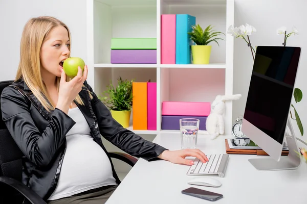 Mulher grávida comendo maçã no escritório — Fotografia de Stock