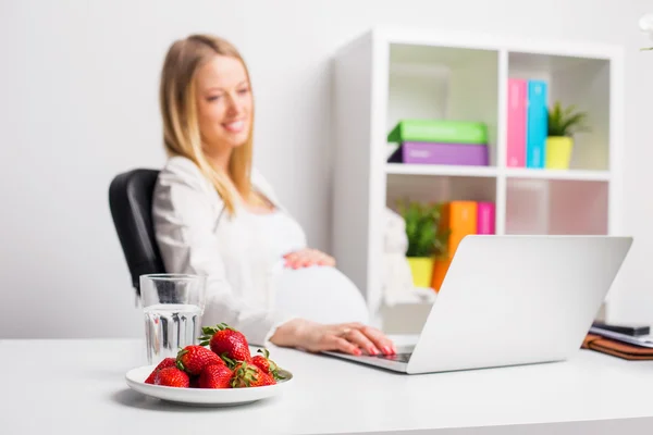 Mulher grávida no escritório com morangos — Fotografia de Stock
