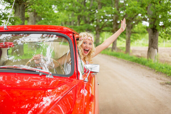 Happy and excited woman hanging out of vintage car