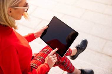 Kadın dışarıda oturuyor ve tablet kullanıyor.