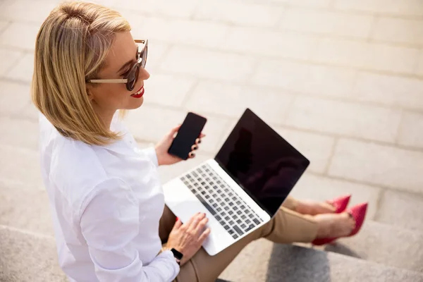 女商人坐在室外使用笔记本电脑和手机 — 图库照片