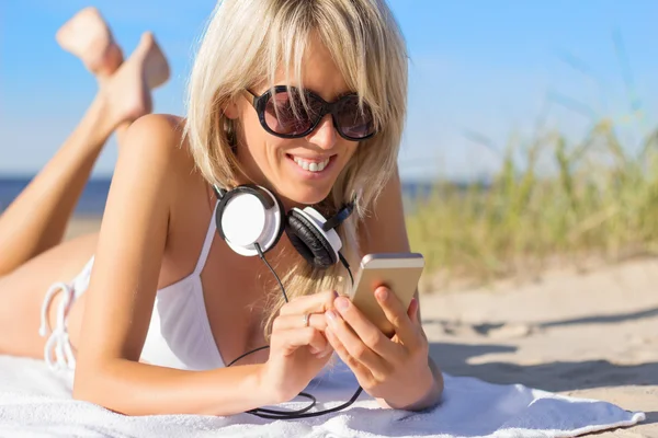 Jonge vrouw met behulp van mobiele telefoon en hoofdtelefoon dragen op het strand — Stockfoto