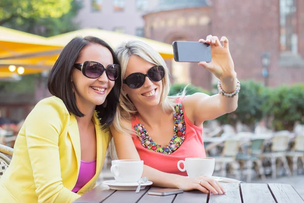 两个漂亮的女人，坐在露天咖啡馆用手机拍照合影 — 图库照片