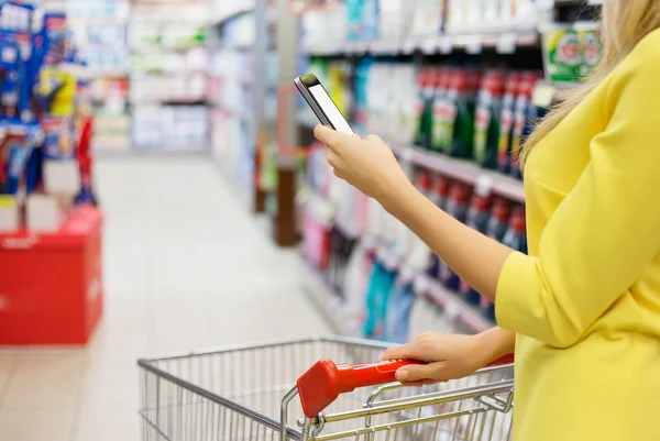 Frau checkt Einkaufsliste auf ihrem Smartphone im Supermarkt — Stockfoto