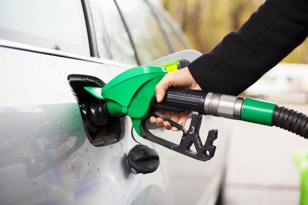 Close-up photo of hand holding fuel pump and refilling car at petrol station