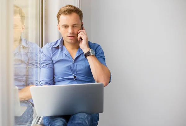 Jonge creatieve man aan het werk met computer tijdens het gesprek op de telefoon — Stockfoto