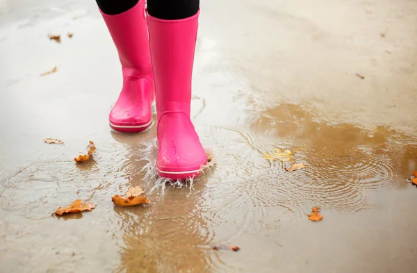 Mujer con botas de goma rosa caminando a través del charco en otoño — Foto de Stock