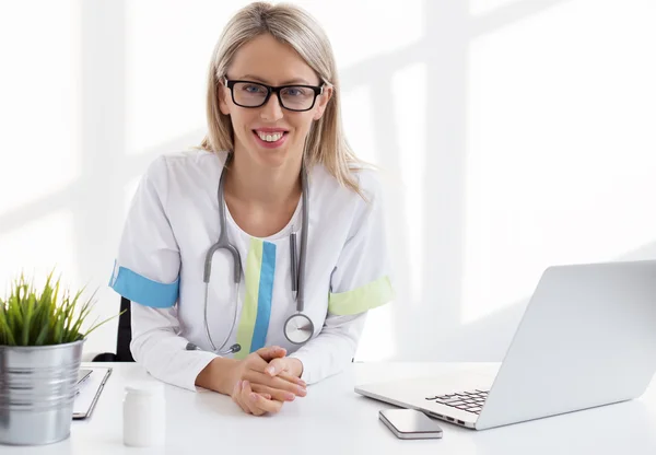 Joven doctora sentada en el escritorio de su consultorio en la clínica — Foto de Stock