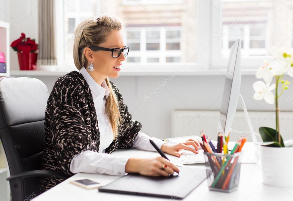 Young female designer using graphics tablet while working with computer