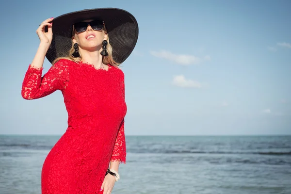 Módní žena s černými letní klobouk a červené šaty na pláži — Stock fotografie