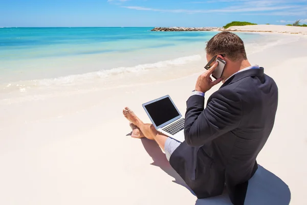 Businessman working with computer and talking on phone on the beach — Stock Photo, Image