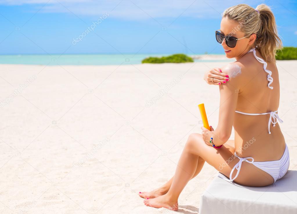 Woman sunbathing on the beach and applying sun protection cream