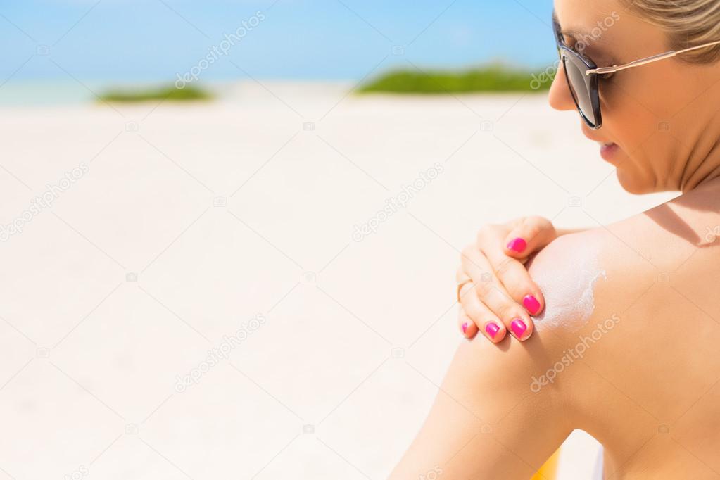 Woman applying sunscreen at the beach on hot summer day