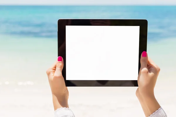Женщина держит планшетный компьютер с пустым экраном на пляже — стоковое фото