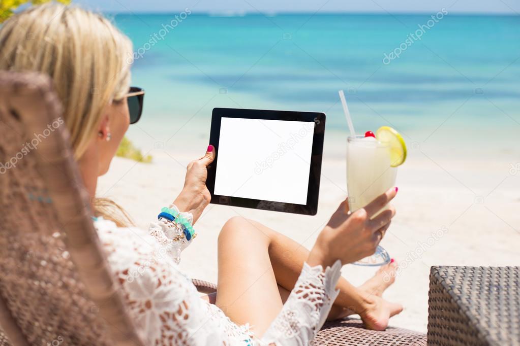 Young woman relaxing on a beach with cocktail and tablet