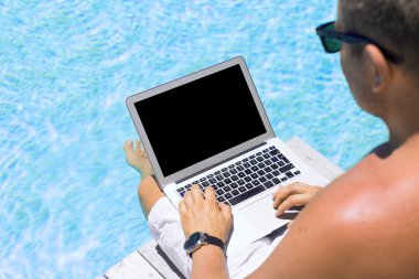 Young man working with laptop computer by the swimming pool