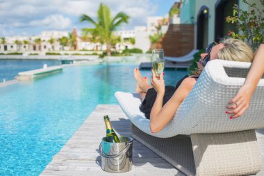 Lady relaxing in deck chair by the pool and drinking champagne clipart