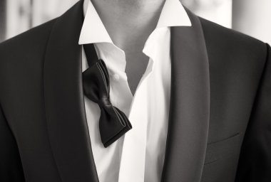 Close-up photo of man in tuxedo with open shirt and loose bow tie clipart